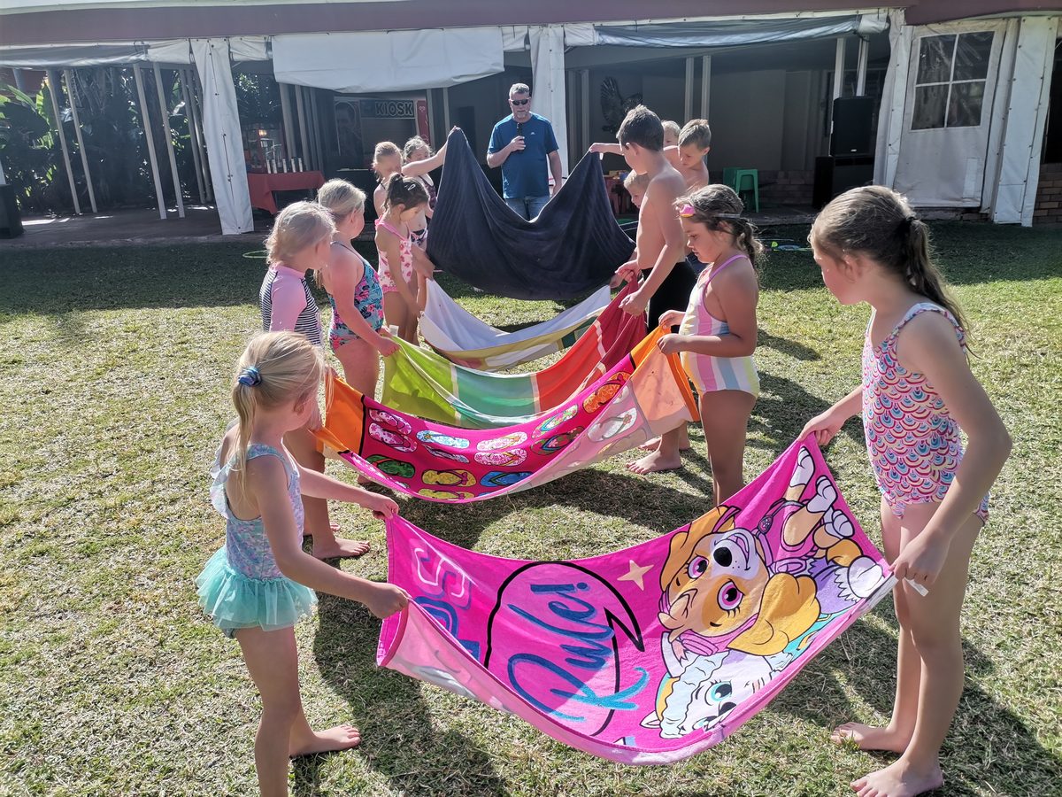 Children playing a towel relay game on the lawn at a holiday resort