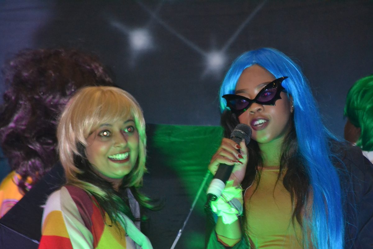 Guest in a blue wig singing karaoke on stage at a themed party