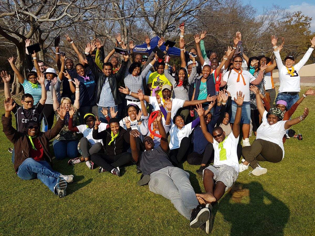 Large corporate team cheering with arms raised after an outdoor team building day