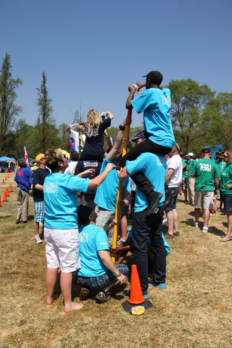 Teams supporting each other during an outdoor pole climb challenge